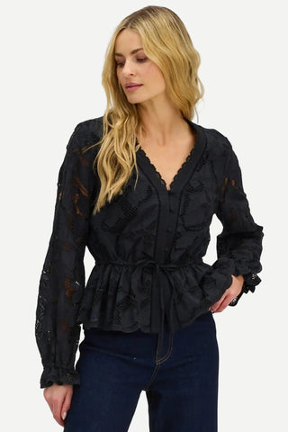A woman wearing a black lace long-sleeve blouse with a scalloped V-neckline and a drawstring waist, paired with dark blue jeans, against a plain white background.