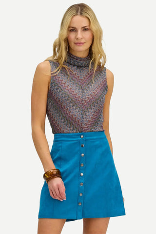 A woman modeling a sleeveless mock-neck top with a multicolor chevron pattern and a bright blue button-front mini skirt, against a plain white background.